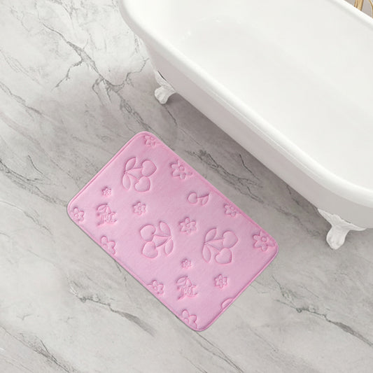 A pink rectangular Quilted Memory Foam Bath Mat with embossed floral and leaf patterns sits on a light gray marble floor beside a white clawfoot bathtub, adding style and offering a skid-resistant surface.