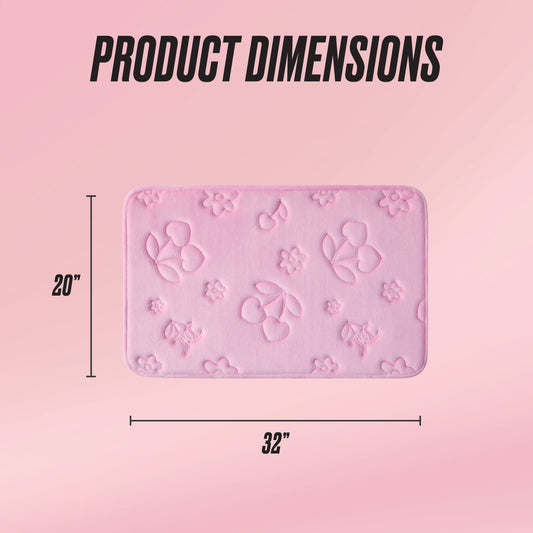 A rectangular Quilted Memory Foam Bath Mat in pink, featuring embossed floral and cherry designs and skid resistance, is shown. It measures 20" x 32". The background has a light pink gradient with Product Dimensions displayed above.