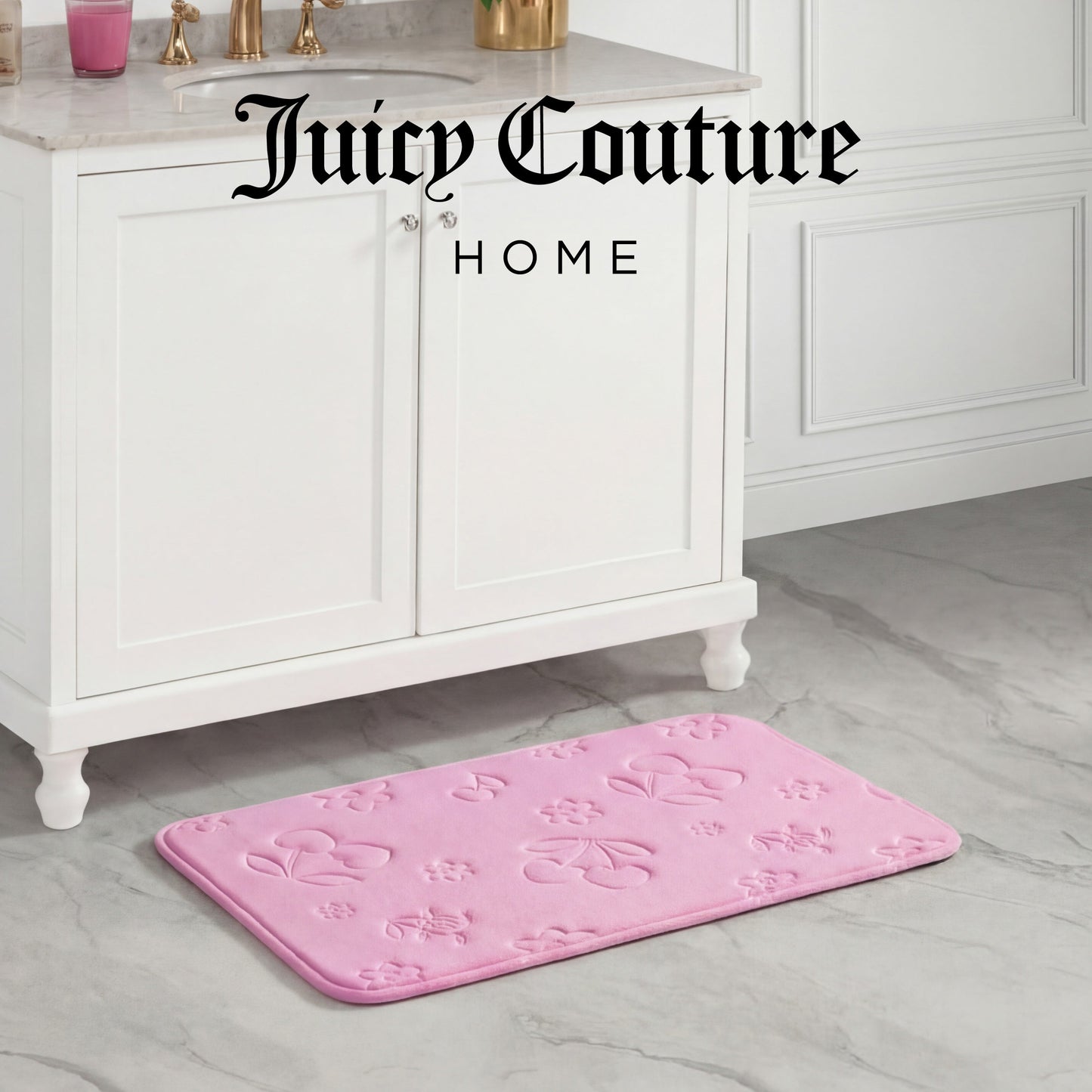 A Quilted Memory Foam Bath Mat in pink with embossed floral and bow designs lies on a marble bathroom floor by a white vanity. The skid-resistant mat adds safety, while Juicy Couture HOME is displayed at the top of the image.