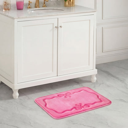 A Quilted Memory Foam Bath Mat, 17" x 24", in plush pink with decorative bows sits on a gray marble floor, complementing the white vanity and gold faucets.
