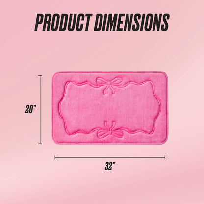 The Quilted Memory Foam Bath Mat, 20" x 32", in pink features decorative bow patterns and a rectangular, quilted design. It is displayed on a pink gradient background with "Product Dimensions" shown above.