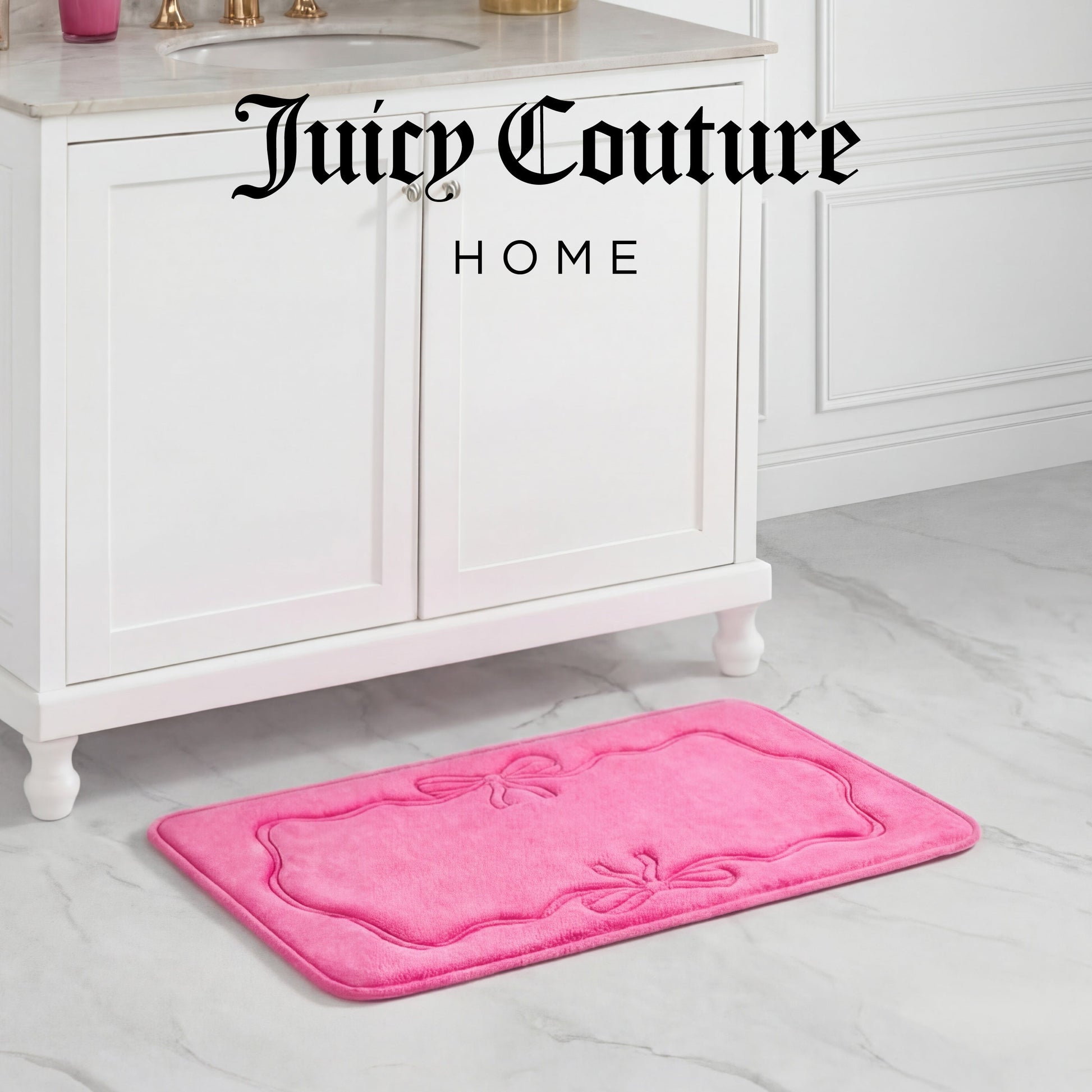 A bright pink Quilted Memory Foam Bath Mat, 20" x 32", featuring a bow design, sits in front of a white bathroom vanity. The stylish, skid-resistant mat adds elegance to the minimalistic decor with "Juicy Couture HOME" above the vanity.