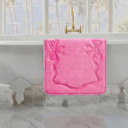 A pink Quilted Memory Foam Bath Mat, 20" x 32", hangs over the side of a white clawfoot tub in a bright bathroom with marble floors and large windows showcasing palm trees outside.