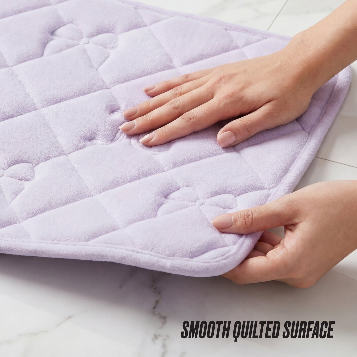 A person touches a soft light purple Quilted Memory Foam Bath Mat 2-Piece Set with a floral pattern on a white tiled floor. The text SMOOTH QUILTED SURFACE appears in the bottom right corner.