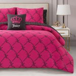 A bed dressed in the Link Printed Bed in a Bag Bedding Set, featuring black chain and JC patterns, is topped with a black pillow showing a pink crown and "Juicy." A white nightstand and lamp sit next to the bed, creating a luxurious atmosphere.