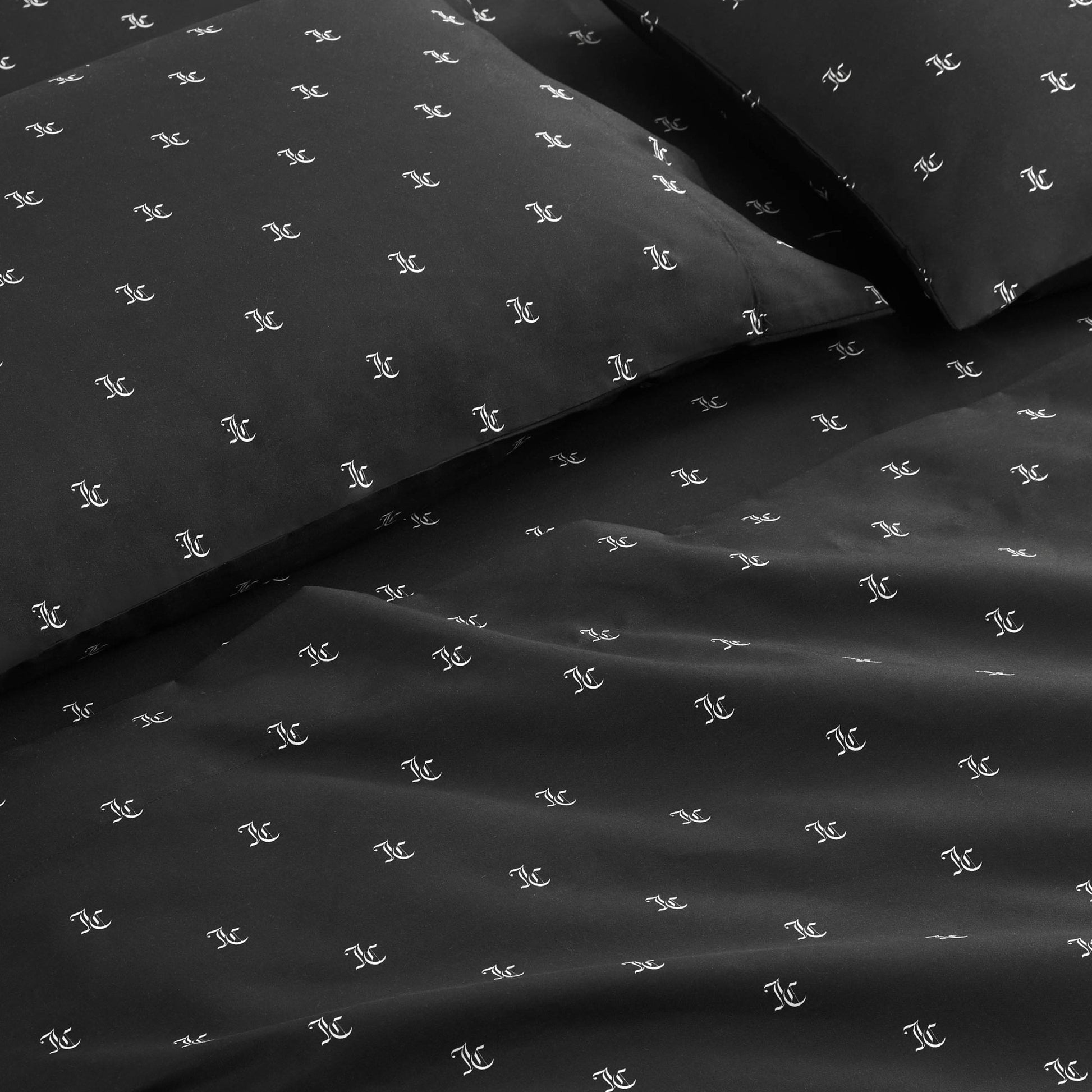 A close-up of the Link Printed Bed in a Bag Bedding Set shows black sheets and pillowcases with a repeating small white logo pattern, neatly arranged on a bed for a luxurious look.