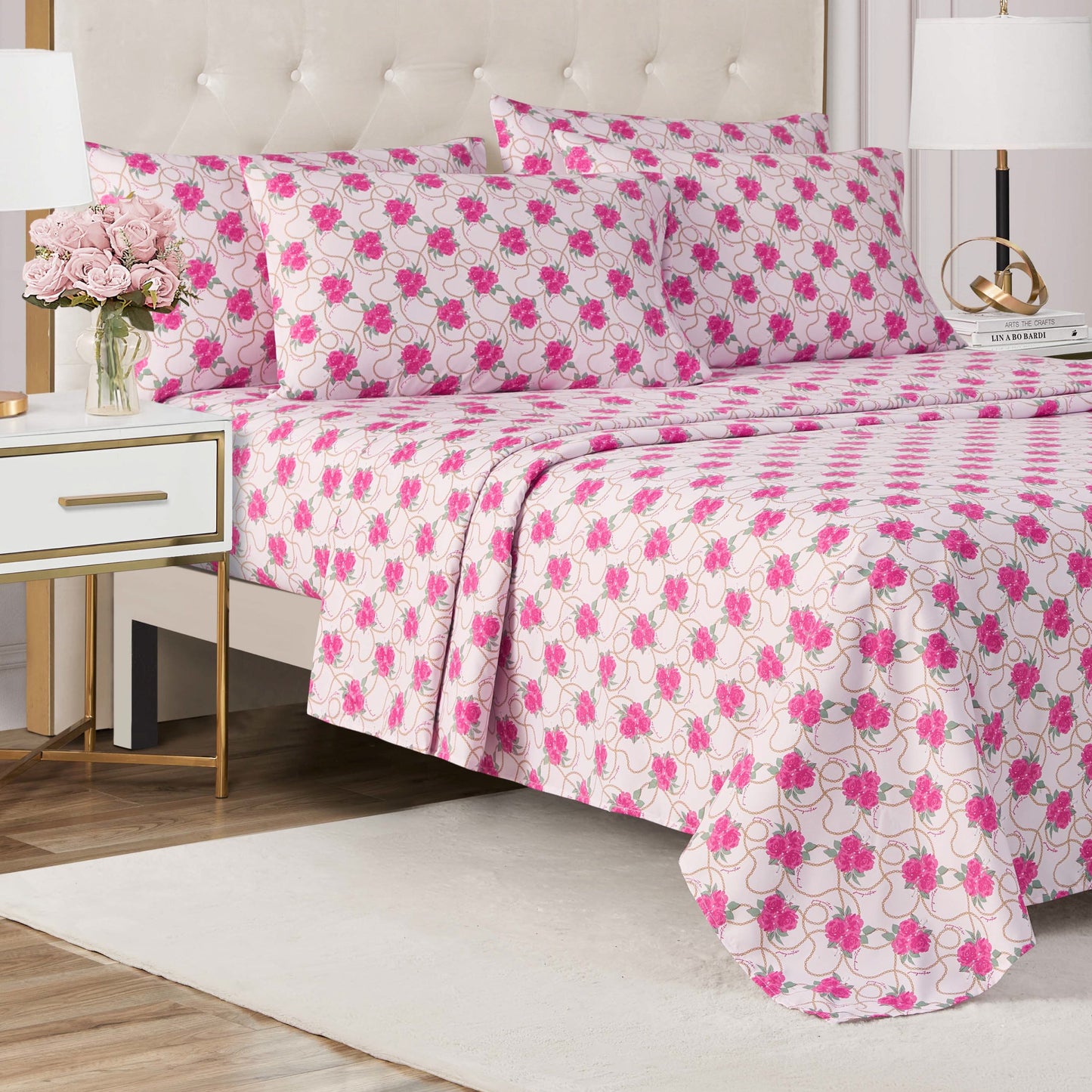 A neatly made bed with a pink and white floral-patterned Microfiber Sheet Set With Extra Pillowcases in a modern bedroom featuring a white nightstand, gold lamp, pink flowers in a vase, neutral rug, and wooden floor.