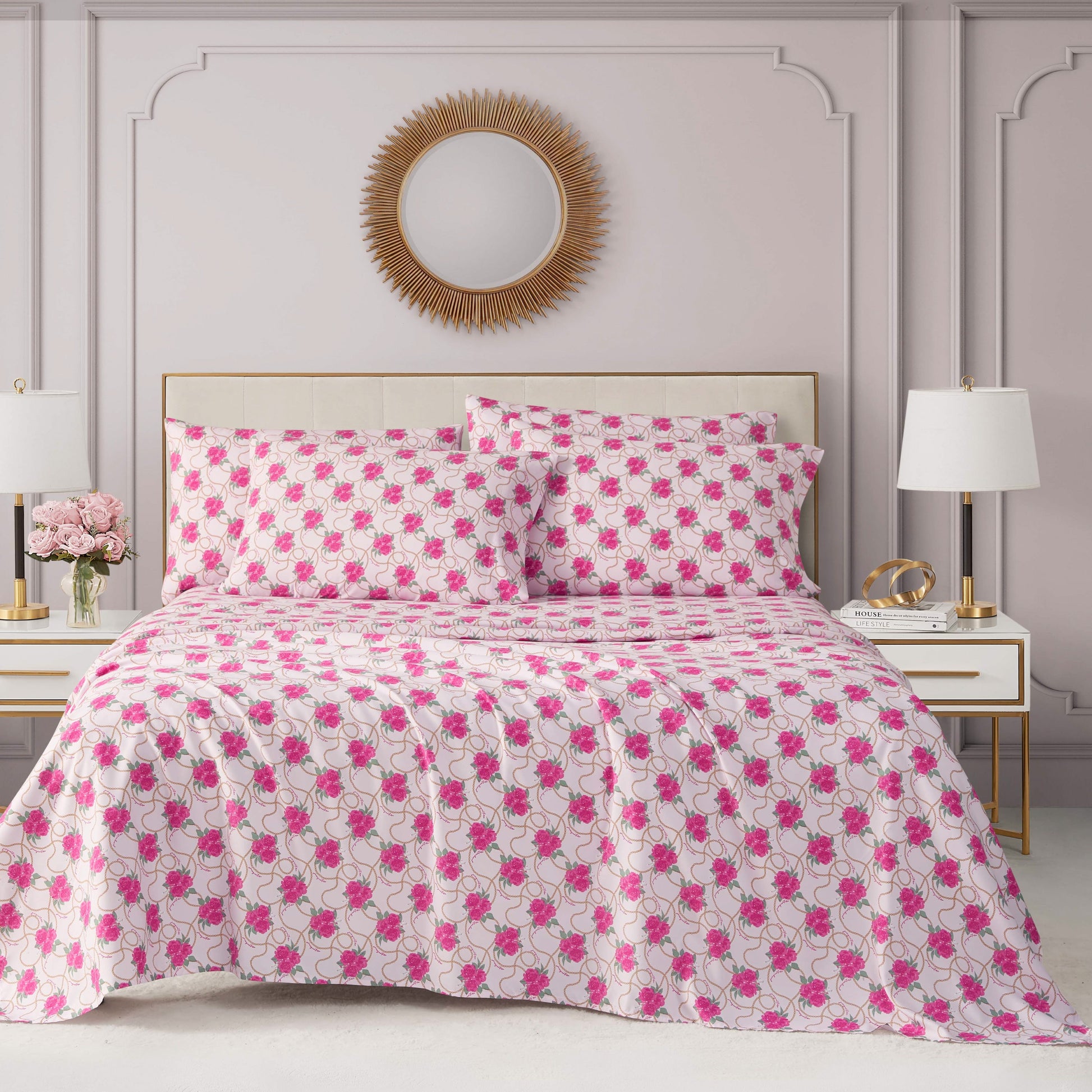 A neatly made bed featuring the Microfiber Sheet Set With Extra Pillowcases is styled with a white and pink floral quilt, matching pillows, and flanked by white nightstands, all set against a light gray wall with decorative molding and a round mirror above.
