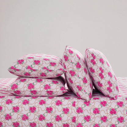 Four pillows with a pink floral pattern are arranged on a matching Microfiber Sheet Set With Extra Pillowcases against a plain white background; two pillows are stacked horizontally, and two are propped upright, all displaying the same vibrant design.