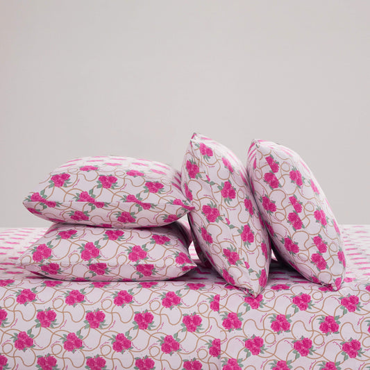 Four pillows with a pink floral pattern are arranged on a matching Microfiber Sheet Set With Extra Pillowcases against a plain white background; two pillows are stacked horizontally, and two are propped upright, all displaying the same vibrant design.