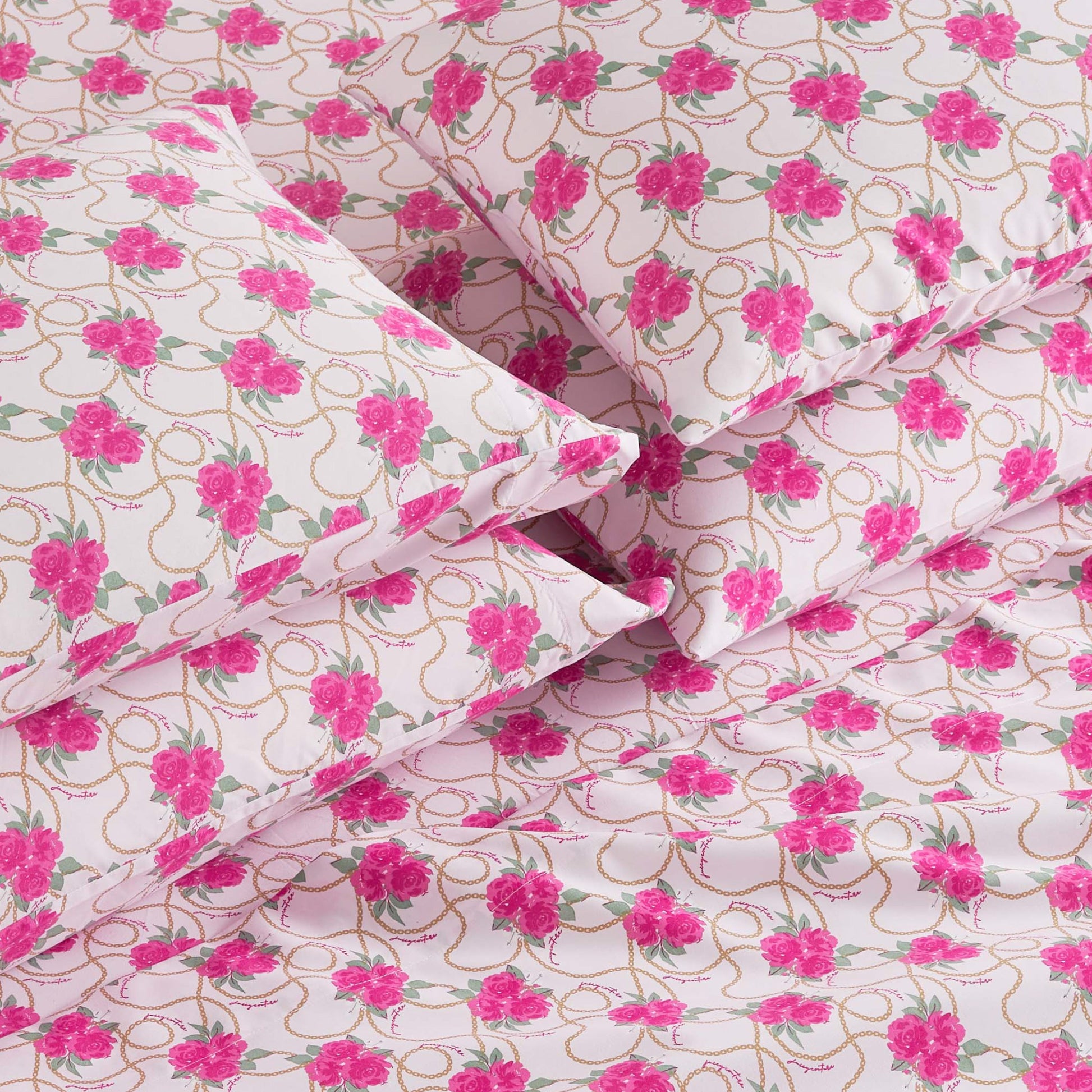A close-up of the Microfiber Sheet Set With Extra Pillowcases, featuring neatly arranged pillows and sheets in a pink floral pattern with green leaves and gold loops on white, giving a luxurious bedding appearance.