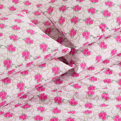 A close-up of the Microfiber Sheet Set With Extra Pillowcases, featuring neatly arranged pillows and sheets in a pink floral pattern with green leaves and gold loops on white, giving a luxurious bedding appearance.