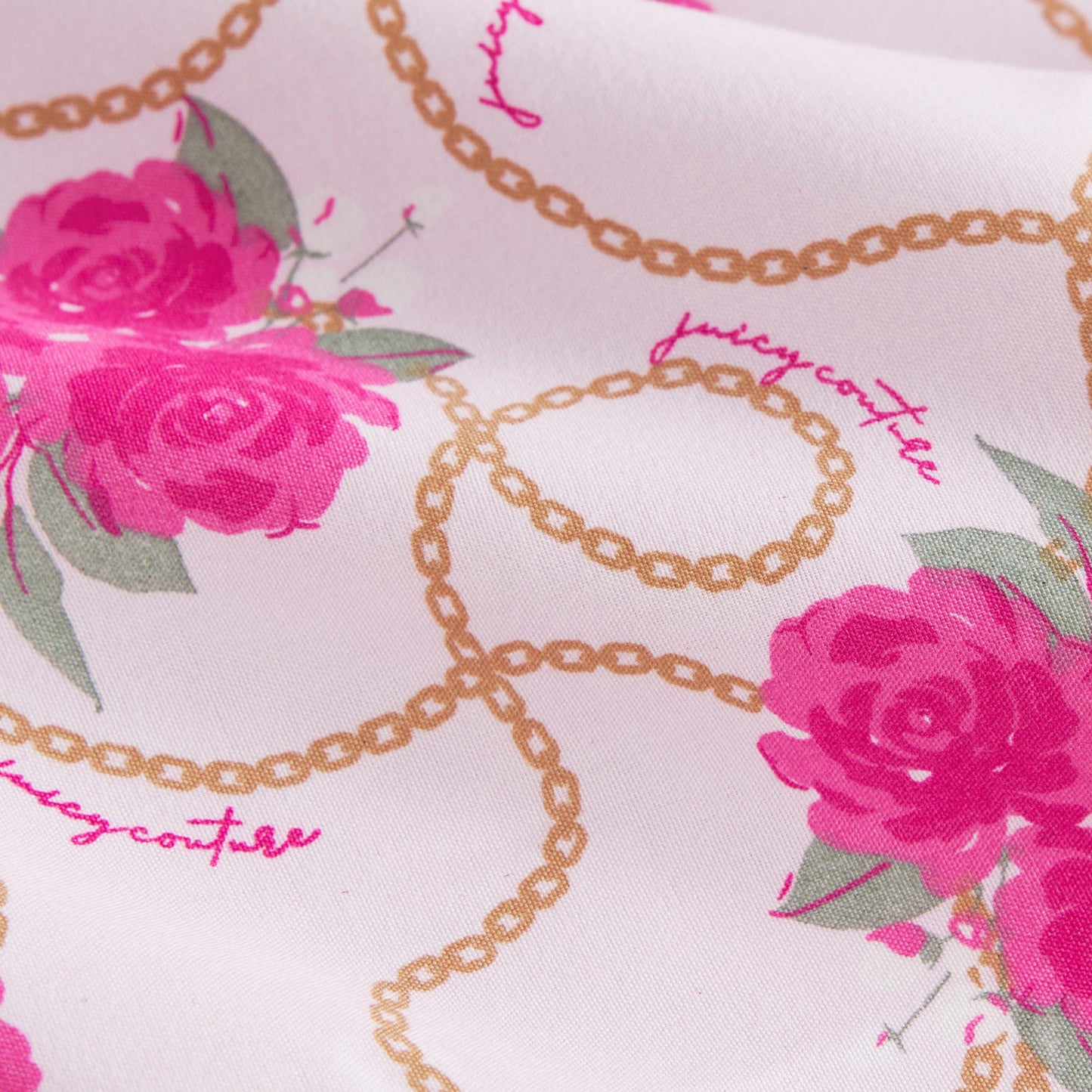 Close-up of pink rose prints and gold chain patterns on the Microfiber Sheet Set With Extra Pillowcases. "Juicy Couture" appears in pink cursive among the designs, adding a touch of luxury bedding style.