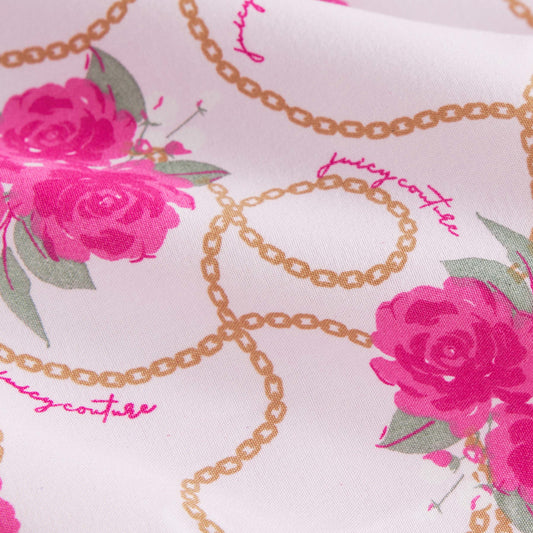 Close-up of pink rose prints and gold chain patterns on the Microfiber Sheet Set With Extra Pillowcases. "Juicy Couture" appears in pink cursive among the designs, adding a touch of luxury bedding style.
