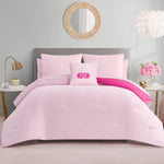 A neatly made bed with the Cherry Reversible Bed in a Bag Bedding Set and decorative pillows, including a monogrammed one in the center. The room features gold accents, a round mirror, flowers, and soft neutral walls.