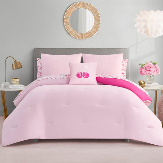 A neatly made bed with the Cherry Reversible Bed in a Bag Bedding Set and decorative pillows, including a monogrammed one in the center. The room features gold accents, a round mirror, flowers, and soft neutral walls.