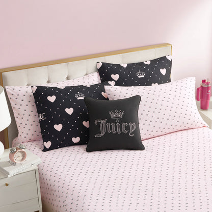 A neatly made bed with the Diamond Hearts Black Comforter Bed in a Bag Set, featuring pink heart-patterned sheets and glam black and pink pillows. A white tufted headboard, pink wall, and nightstand complete the stylish look.