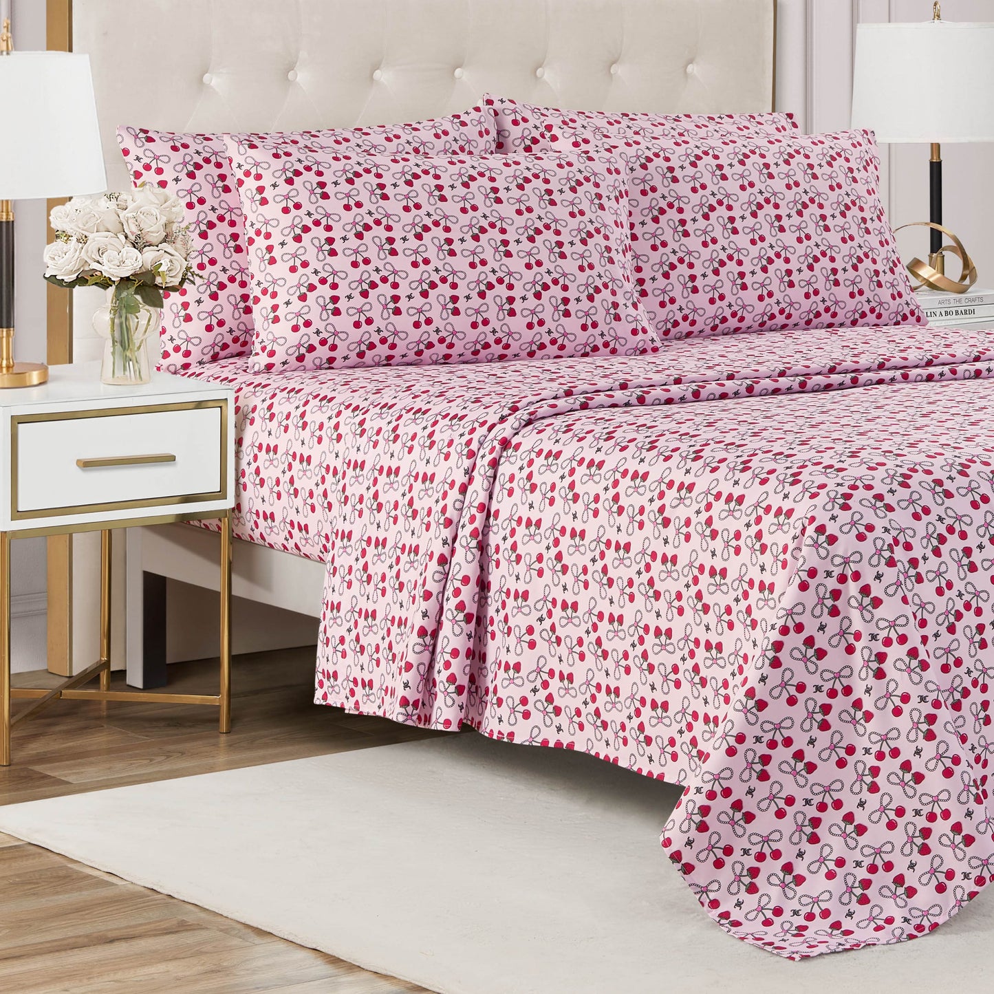 A neatly made bed with a light-colored tufted headboard, dressed in a Microfiber Sheet Set With Extra Pillowcases, sits next to a nightstand with a lamp and vase of white flowers on a white rug.