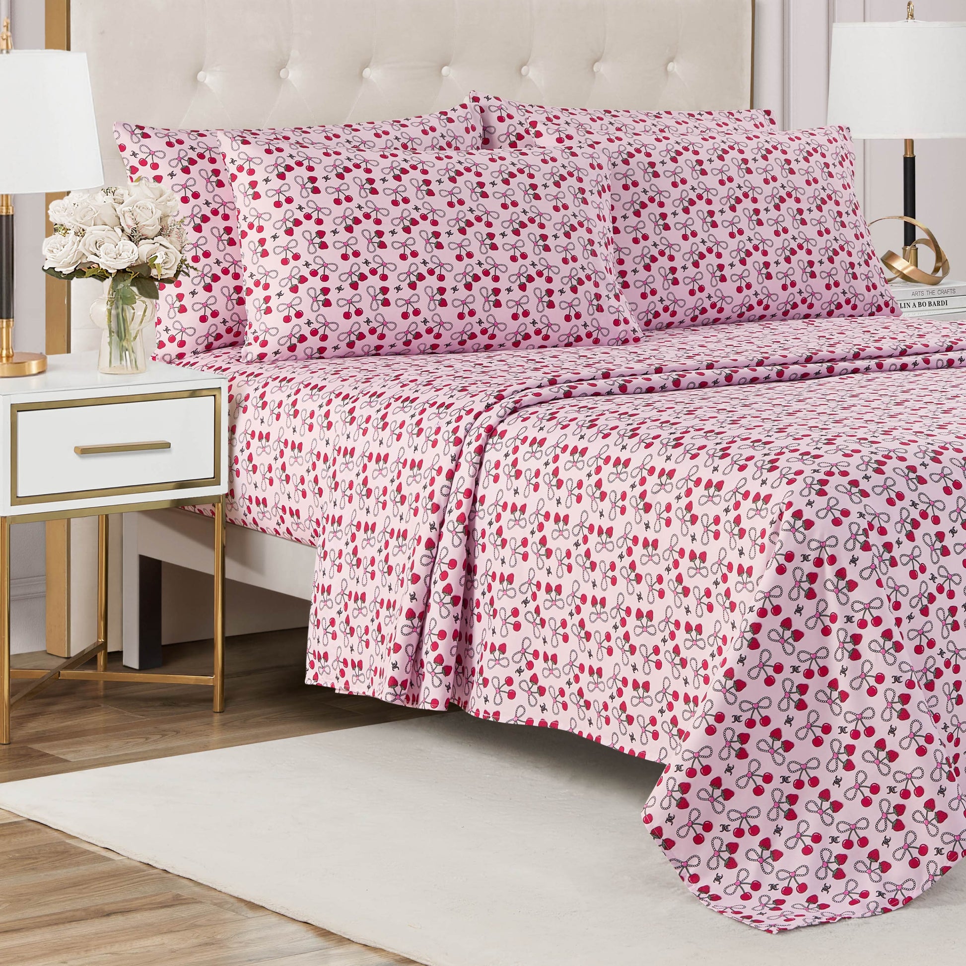 A neatly made bed with a light-colored tufted headboard, dressed in a Microfiber Sheet Set With Extra Pillowcases, sits next to a nightstand with a lamp and vase of white flowers on a white rug.