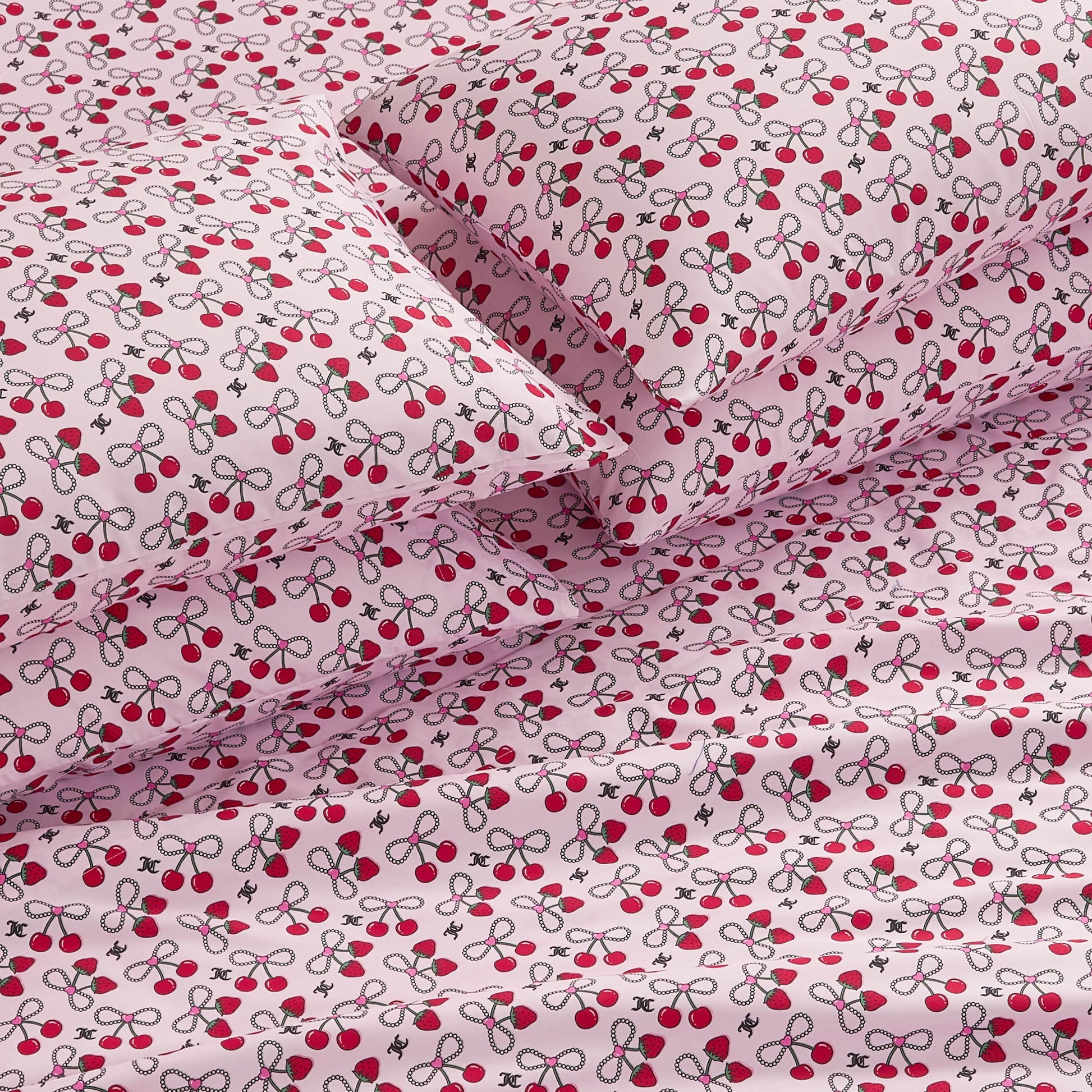 The Microfiber Sheet Set With Extra Pillowcases features pink sheets and pillowcases adorned with a playful pattern of red cherries and green leaves, adding a whimsical, luxurious touch to your bedding.