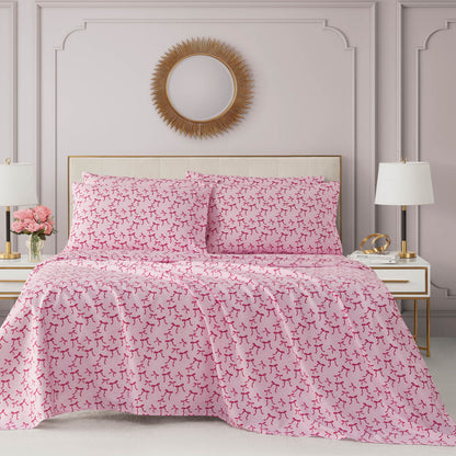 A neatly made bed with a pink and white comforter and pillows, flanked by two white nightstands with lamps and decor. Above the Microfiber Sheet Set With Extra Pillowcases hangs a round mirror with a gold sunburst frame.