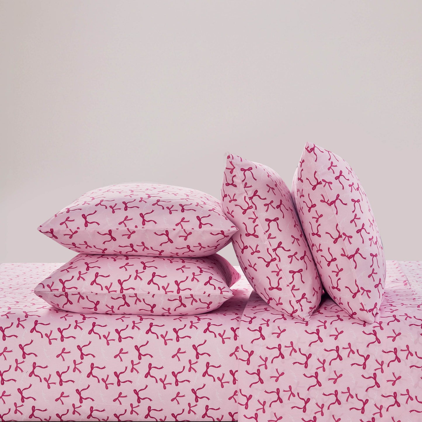 Four pink pillows with red abstract branch-like designs are stacked on a matching pink Microfiber Sheet Set With Extra Pillowcases, creating a stylish and luxurious bedding display against a plain light background.