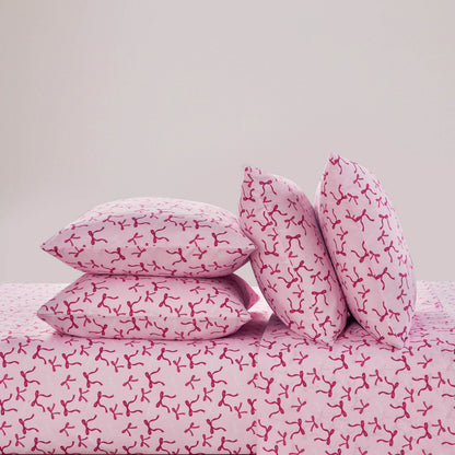 Four pink pillows with red abstract branch-like designs are stacked on a matching pink Microfiber Sheet Set With Extra Pillowcases, creating a stylish and luxurious bedding display against a plain light background.