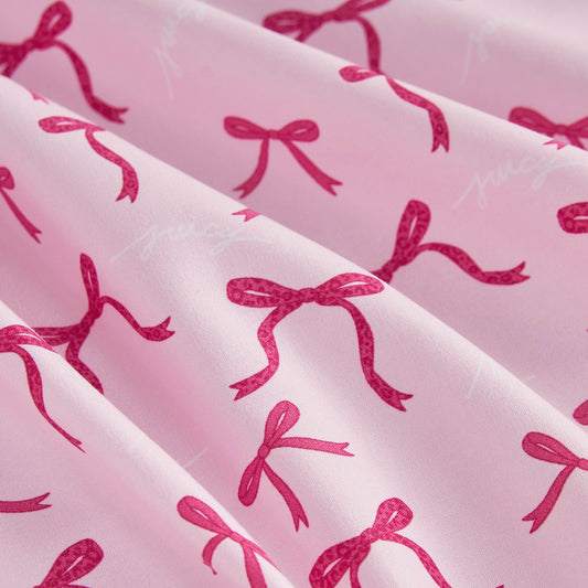 The Microfiber Sheet Set With Extra Pillowcases features light pink sheets with darker pink bows and subtle white "juicy" prints, crafted from soft microfiber that drapes beautifully for a playful touch to your bedding.