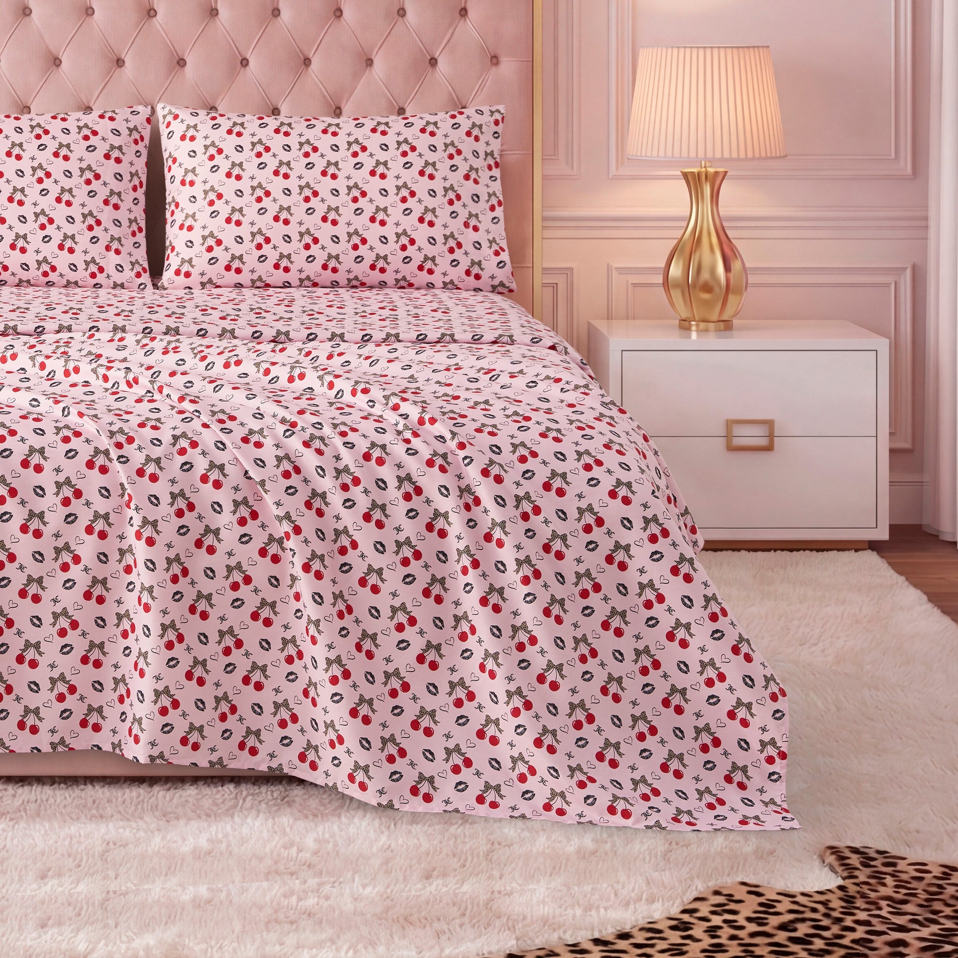 A neatly made bed with a light pink tufted headboard, red and black floral luxury bedding, matching pillows, and a Printed Microfiber Sheet Set. Beside the bed are a gold lamp and white nightstand on a plush white rug.