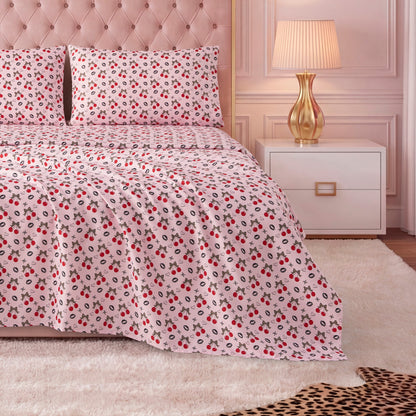A neatly made bed with a light pink tufted headboard, red and black floral luxury bedding, matching pillows, and a Printed Microfiber Sheet Set. Beside the bed are a gold lamp and white nightstand on a plush white rug.