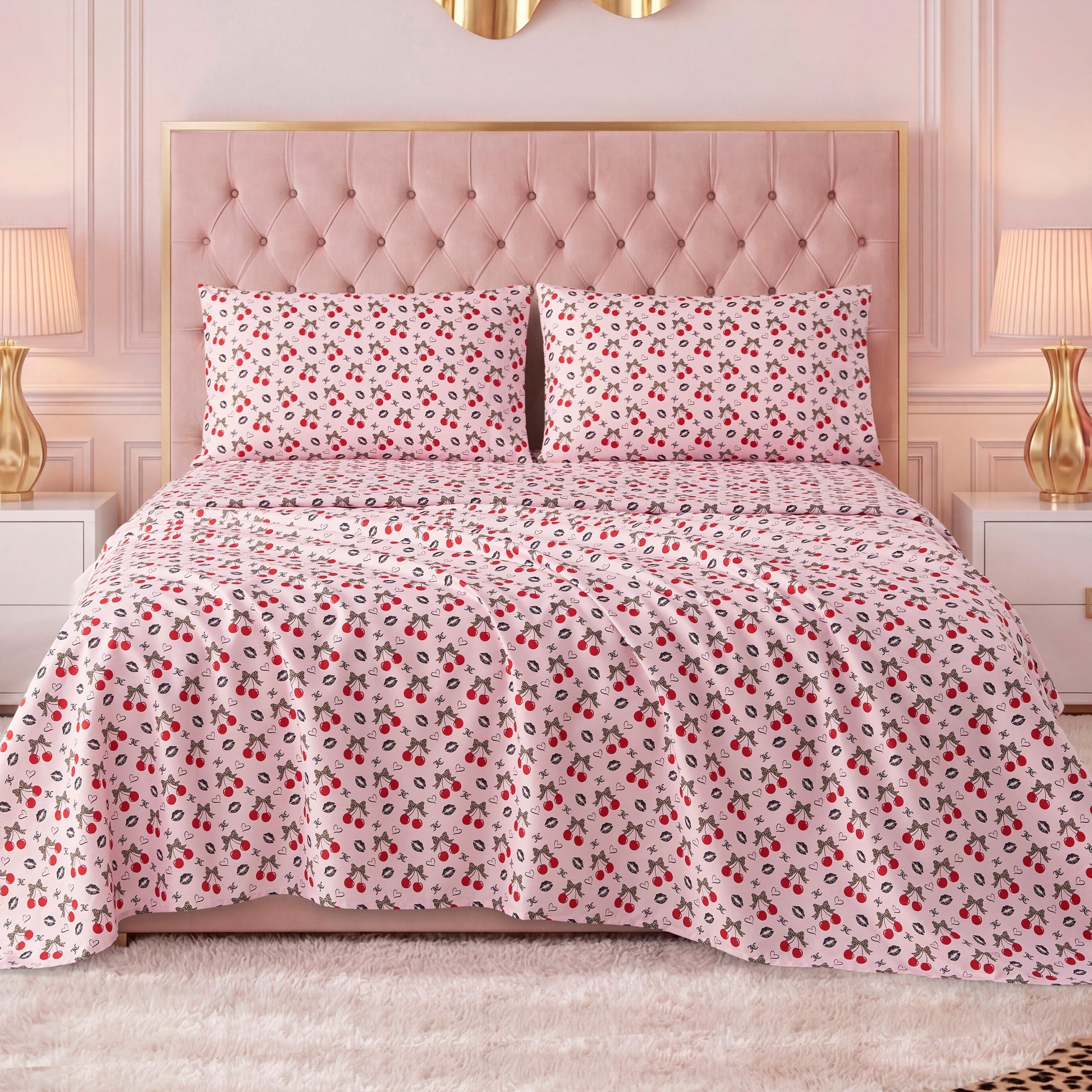 A bed with a tufted pink headboard features a white bedspread with red and black floral designs, paired with a Printed Microfiber Sheet Set, and flanked by white nightstands with gold lamps in a stylish, softly lit bedroom.