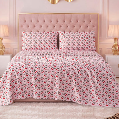 A bed with a tufted pink headboard features a white bedspread with red and black floral designs, paired with a Printed Microfiber Sheet Set, and flanked by white nightstands with gold lamps in a stylish, softly lit bedroom.