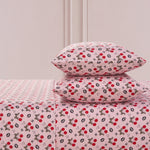 The Printed Microfiber Sheet Set includes two pillows and a sheet, all featuring red cherries, black and white bunnies, hearts, and white flowers on a soft pink background—a playful yet luxurious bedding choice.