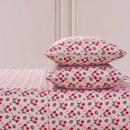 The Printed Microfiber Sheet Set includes two pillows and a sheet, all featuring red cherries, black and white bunnies, hearts, and white flowers on a soft pink background—a playful yet luxurious bedding choice.