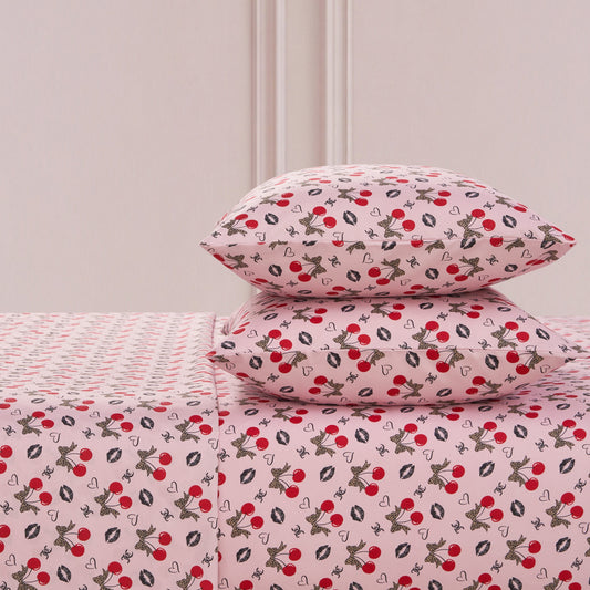 The Printed Microfiber Sheet Set includes two pillows and a sheet, all featuring red cherries, black and white bunnies, hearts, and white flowers on a soft pink background—a playful yet luxurious bedding choice.
