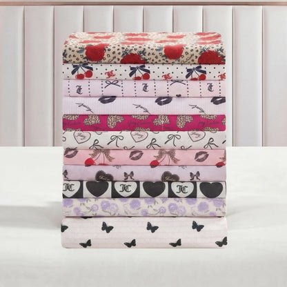 A stack of Printed Microfiber Sheet Sets in pastel colors and playful patterns—hearts, lips, cherries, bows, and butterflies—neatly arranged on a white surface with a pale upholstered headboard in the background.