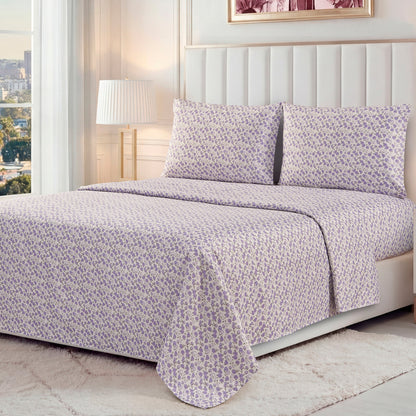 A neatly made bed features the Printed Microfiber Sheet Set in a light purple floral pattern, with matching pillowcases, in a bright modern bedroom with white walls, a large window, lamp, and white rug.
