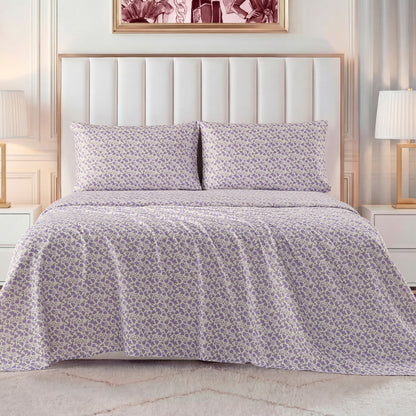 A neatly made bed with a white padded headboard features a light purple and white floral bedspread, matching pillows, and the Printed Microfiber Sheet Set. White nightstands and lamps sit beside the bed, with framed art displayed above.