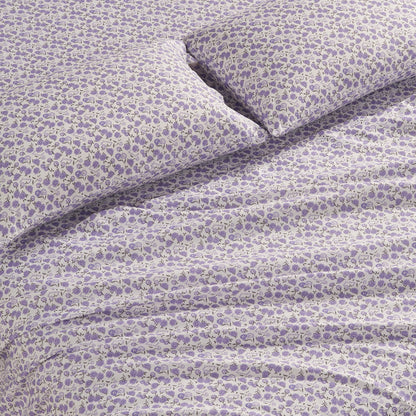 A close-up of a bed featuring the Printed Microfiber Sheet Set, showing a pillow and blanket in matching white fabric with a small purple floral pattern.