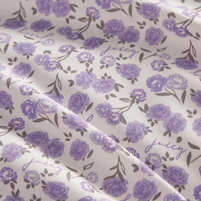 This Printed Microfiber Sheet Set features a white background with purple roses, green leaves, and "juicy" in cursive for a delicate floral look. Softly draped fabric adds a touch of luxury to any bedroom.