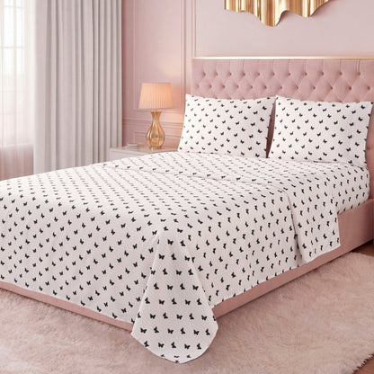 A pink upholstered bed with a tufted headboard features the luxurious Printed Microfiber Sheet Set in white with a small black pattern. Pink walls, gold wall decor, a bedside table with a lamp, and light curtains complete the elegant room.