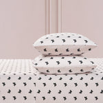 Two white pillows with a black butterfly print are stacked on the Printed Microfiber Sheet Set, set against a light pink wall with decorative molding.