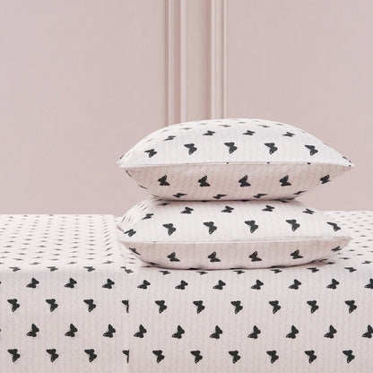 Two white pillows with a black butterfly print are stacked on the Printed Microfiber Sheet Set, set against a light pink wall with decorative molding.