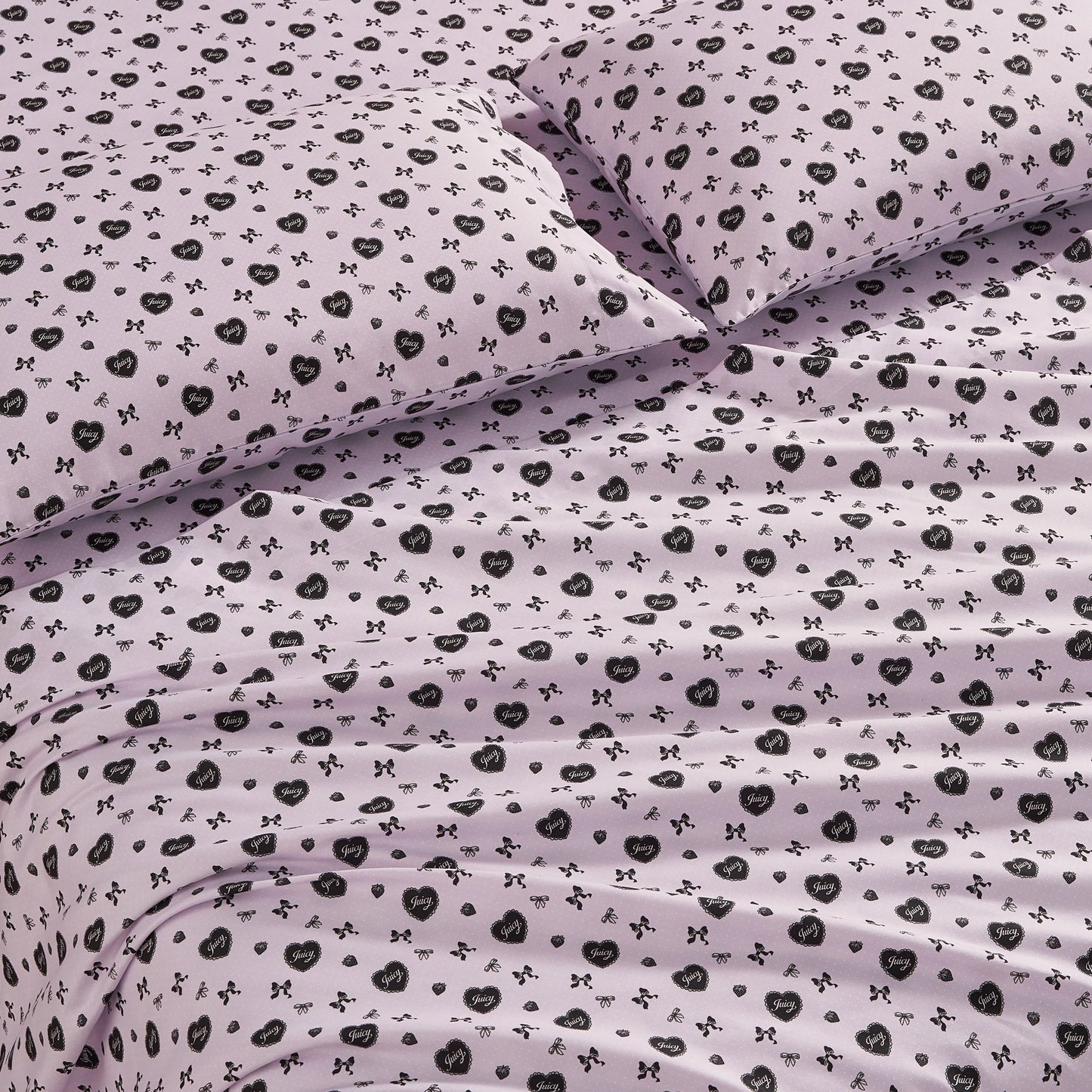 The Printed Microfiber Sheet Set features a light purple color with black floral and bow designs. This luxury bedding includes matching pillows and looks soft, neatly arranged, and inviting with gentle folds and creases.