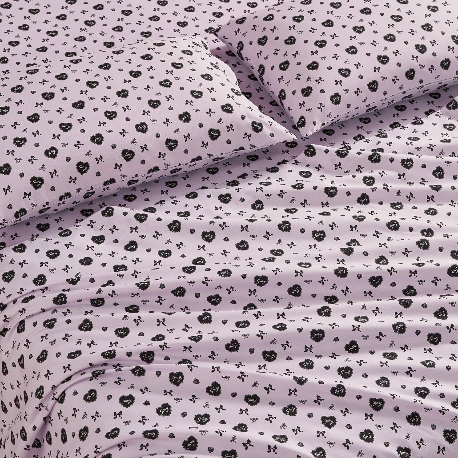 The Printed Microfiber Sheet Set features a light purple color with black floral and bow designs. This luxury bedding includes matching pillows and looks soft, neatly arranged, and inviting with gentle folds and creases.
