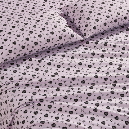 The Printed Microfiber Sheet Set features a light purple color with black floral and bow designs. This luxury bedding includes matching pillows and looks soft, neatly arranged, and inviting with gentle folds and creases.