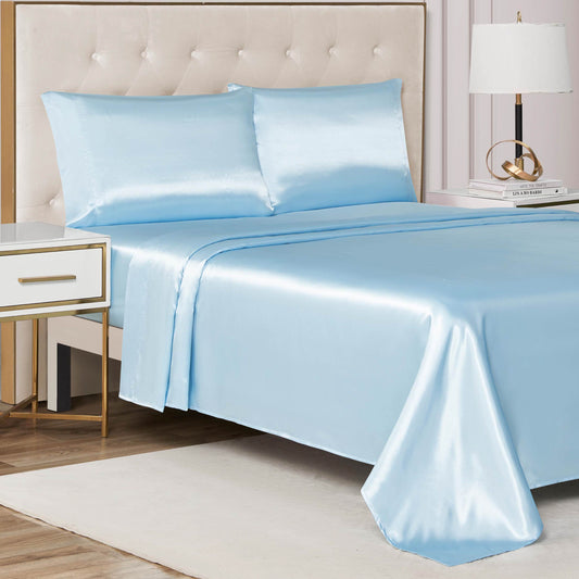A neatly made bed features the Solid Satin Sheet Set in shiny light blue with matching pillowcases, set against a tufted beige headboard. Next to the bed is a white nightstand with a lamp and books on a light-colored rug.
