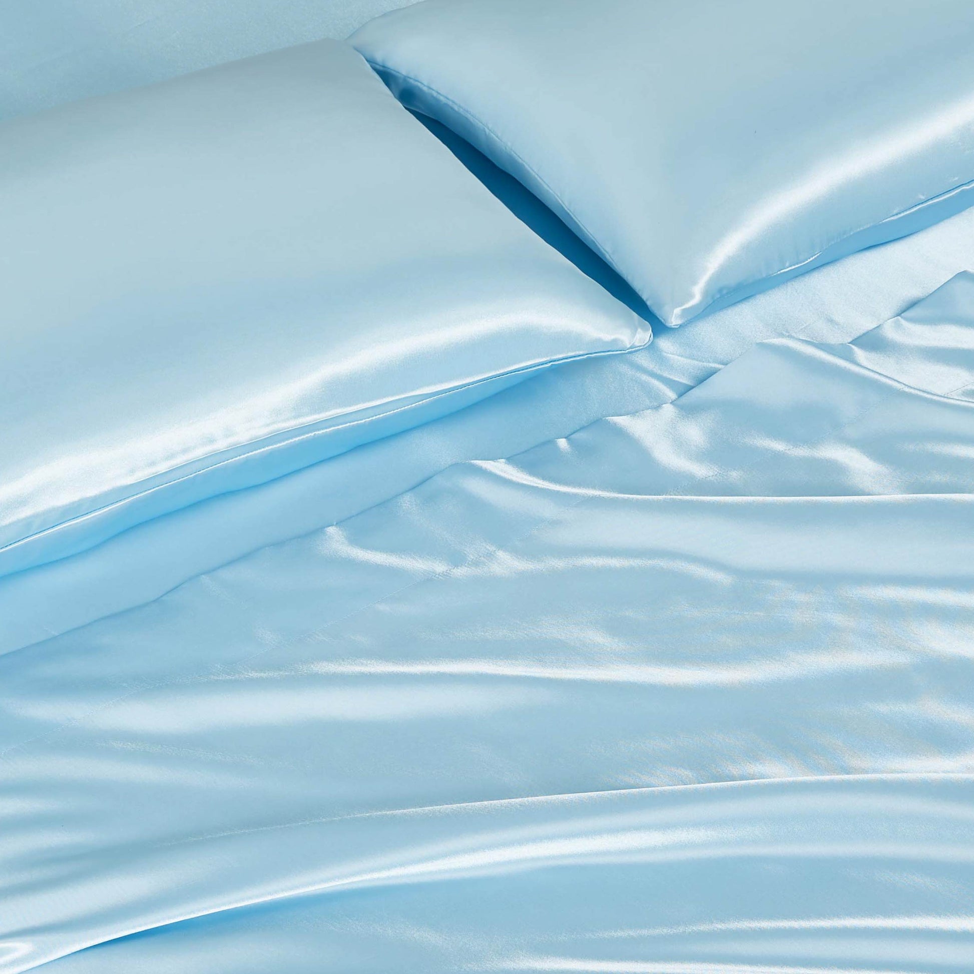 Close-up of the Solid Satin Sheet Set in light blue, featuring ultra-soft satin sheets and two matching pillowcases with a smooth, shiny surface and soft folds for a luxurious look.