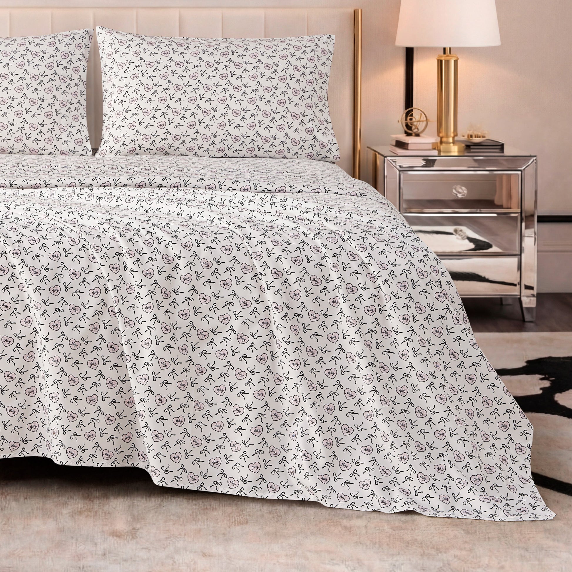 A neatly made bed with the Printed Microfiber Sheet Set in white and small floral patterns, paired with a mirrored nightstand holding a lamp, books, and decor, creates an inviting modern bedroom with luxurious bedding accents.