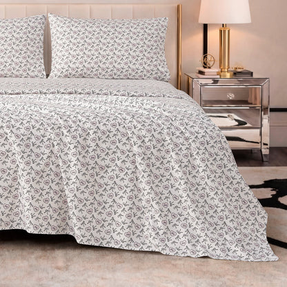 A neatly made bed with the Printed Microfiber Sheet Set in white and small floral patterns, paired with a mirrored nightstand holding a lamp, books, and decor, creates an inviting modern bedroom with luxurious bedding accents.
